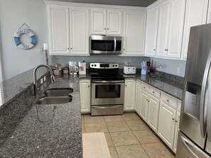 A kitchen with white cabinets, a stainless steel refrigerator, a microwave, an oven, and a sink. - Pier Pleasure - Surfside Beach (Surfside Beach)