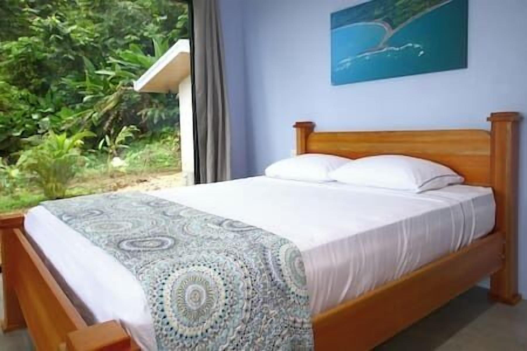 Une chambre avec un lit, une fenêtre donnant sur un paysage verdoyant et un tableau accroché au mur.