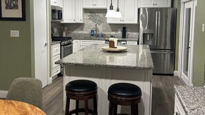 Una cocina moderna con armarios blancos, encimera de granito, refrigerador de acero inoxidable y ventilador de techo.