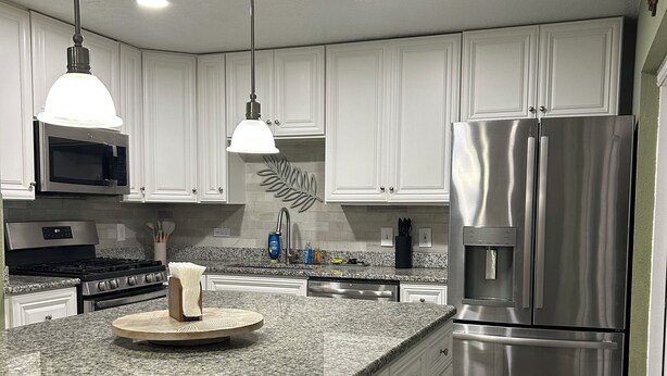 Una cocina moderna con armarios blancos, encimeras de granito, electrodomésticos de acero inoxidable e iluminación colgante.