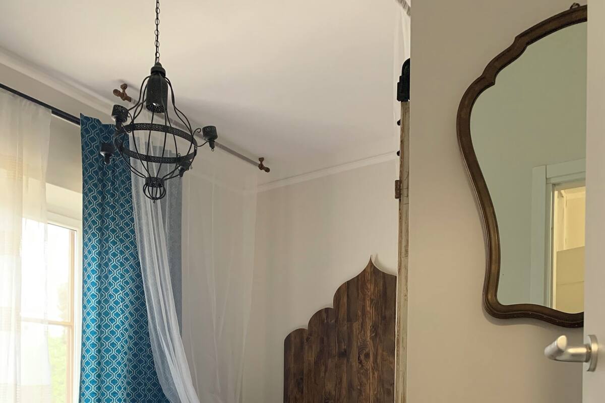 A bedroom with a wooden headboard, a bed with patterned pillows, a bedside table with a tray, and a hanging lamp.