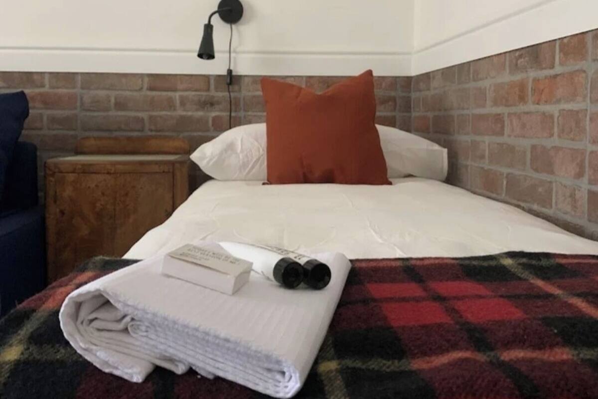 A neatly made bed with a plaid blanket, a pillow, and a book on the bed.