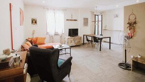 A living room with a sofa, a dining table, a TV, and a dreamcatcher on the wall.