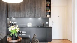 Una cocina moderna con armarios de madera oscura, una encimera negra, una tetera blanca y un jarrón con flores blancas sobre una mesa de madera.