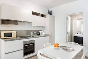 A modern kitchen with white cabinetry, a microwave, a coffee maker, and a dining table with a magazine and fruit. - Joy of Rome Trastevere | Balcony | Kitchen (Rome)