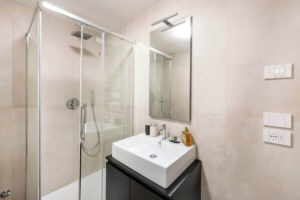 Une salle de bain moderne avec une douche à parois de verre, un lavabo blanc et un miroir au-dessus.