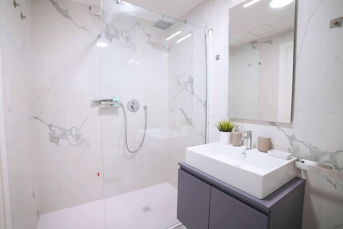 Un bagno moderno con doccia vetrata, un lavandino bianco su un piano in marmo e uno specchio grande sopra il lavandino.