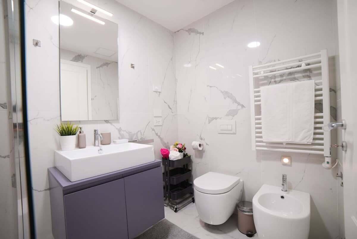 Ein modernes Badezimmer mit weißer Marmorwand, einem großen Spiegel, einem weißen Waschbecken, einer Toilette und einem Bidet.