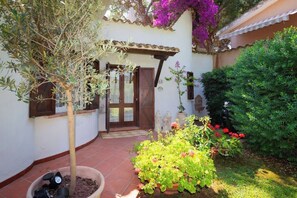 A courtyard with a small tree, a potted plant with red flowers, and a tiled patio. - Villa Gioia | Tranquil Hideaway Beach Cottage (Pula)