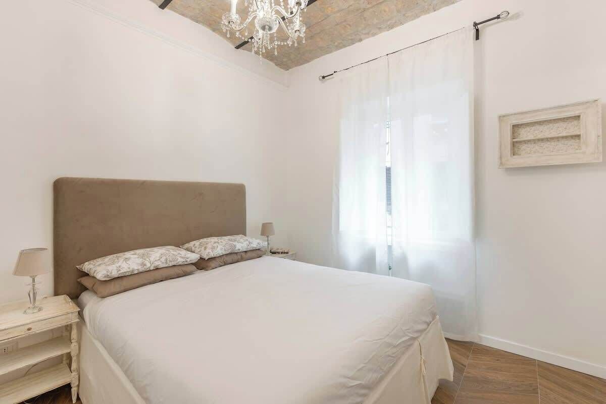 A bedroom with a large bed, a nightstand, a lamp, and a chandelier.