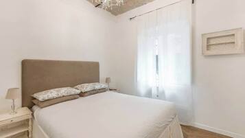 A bedroom with a large bed, a nightstand, a lamp, and a chandelier.