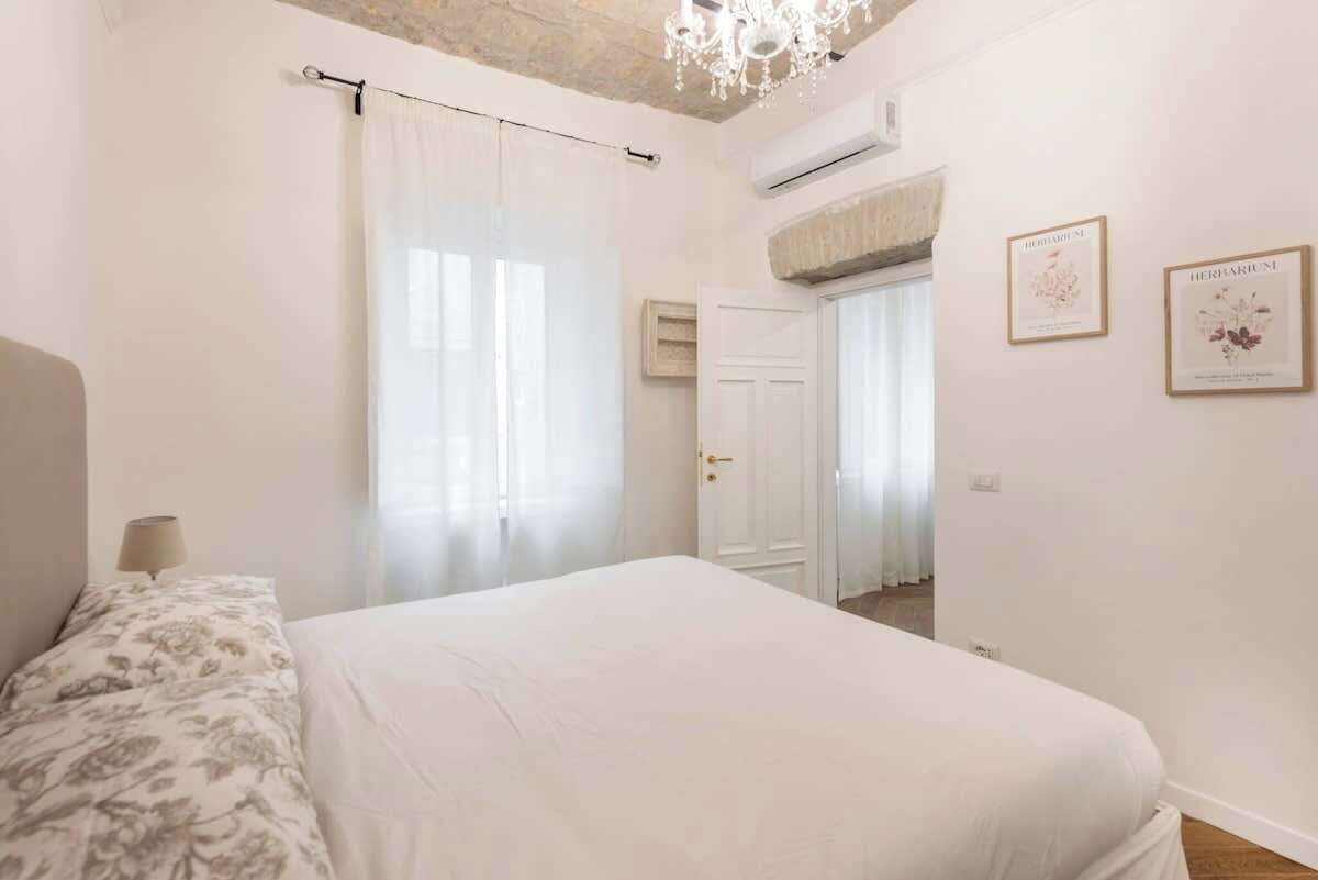 A bedroom with a bed, a chandelier, a door, and framed pictures on the wall.