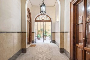 A hallway with a tiled floor, a wooden door on the right, and a large arched window at the end.