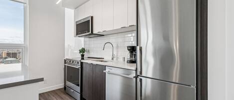 Une cuisine moderne dotée d’appareils électroménagers en acier inoxydable, de meubles blancs et offrant une vue sur la ville.