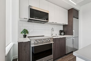 A modern kitchen with a built-in oven, a microwave, a coffee maker, and a refrigerator. - Cozy 1-Bedroom in Calgary | BLVD Beltline (Calgary)