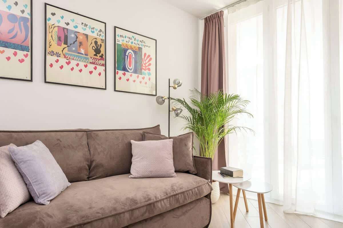 A living room with a brown sofa, a potted plant, and three framed artworks on the wall.