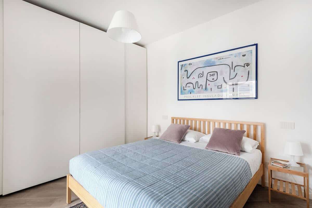 Una camera da letto con un letto, comodini, una lampada a sospensione e un'opera d'arte appesa al muro.