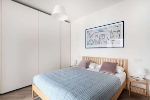 Een slaapkamer met een bed, nachtkastjes, een hanglamp en een wanddecoratie.