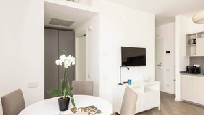 A modern living room with a round dining table, a flat-screen TV mounted on the wall, and a kitchen area with white cabinetry. - Casa di Miranda by Trastevere (Rome)