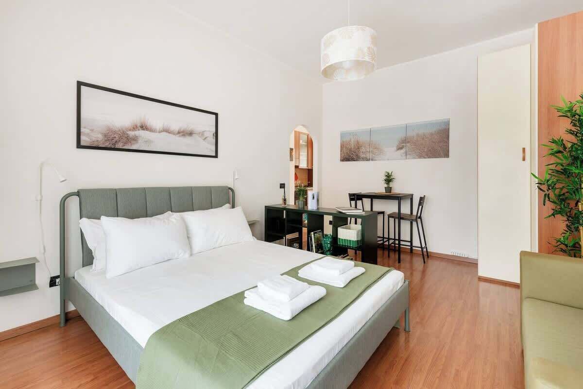 A hotel room with a bed, desk, chair, and a plant.