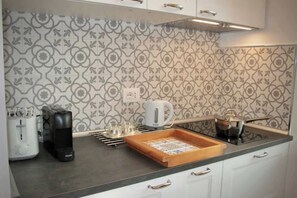A kitchen with a patterned backsplash, a coffee maker, a kettle, and a tray.