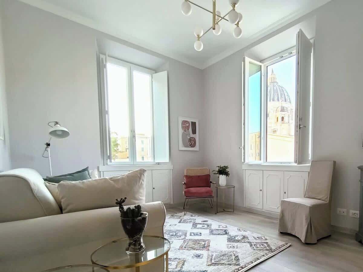 Un salon moderne avec un canapé, une petite table et un fauteuil. Il y a deux fenêtres donnant sur un immeuble.