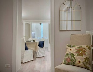 A room with a dining area, a chair with a floral cushion, and a mirror on the wall.