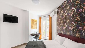 A hotel room with a bed, a desk, a chair, a television, and a large floral wall. - Aria di Trastevere | 3BR | 3BATH | (Rome)