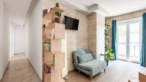 A modern living room with a sofa, a TV mounted on the wall, and a wooden bookshelf. - Aria di Trastevere | 3BR | 3BATH | (Rome)