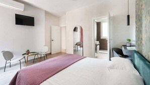 Moderni hotellihuone, jossa on suuri sänky, seinälle asennettu taulutelevisio, työpöytä tuolilla ja peili.
