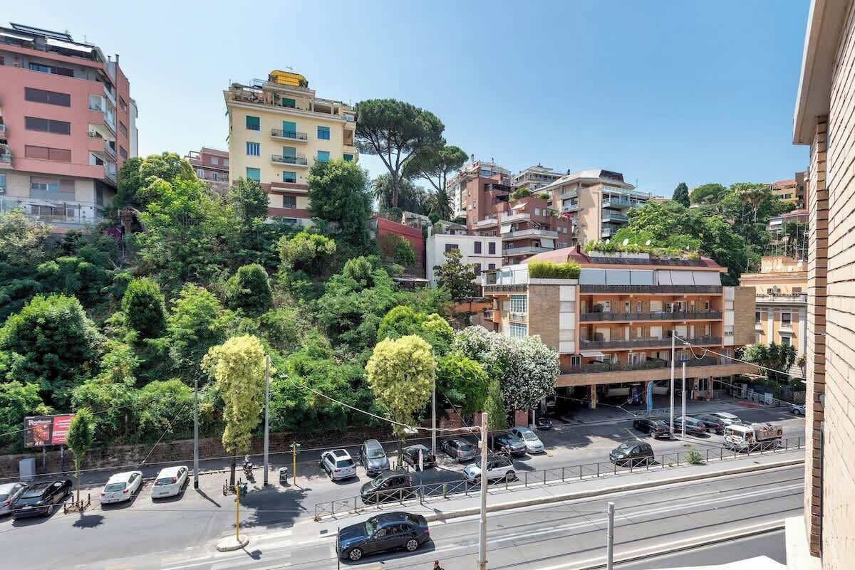 Un edificio de varios pisos con balcones, un estacionamiento y una vista de la calle con autos y árboles.