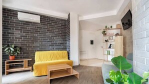 A modern living room with a yellow sofa, wooden coffee table, and a brick accent wall. - Aria di Trastevere | Double Bedroom "2" en suite (Rome)