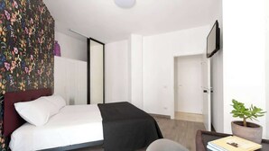 A bedroom with a bed, a chair, a bedside table with a book, a potted plant, and a television on the wall. - Aria di Trastevere | Double Bedroom "2" en suite (Rome)