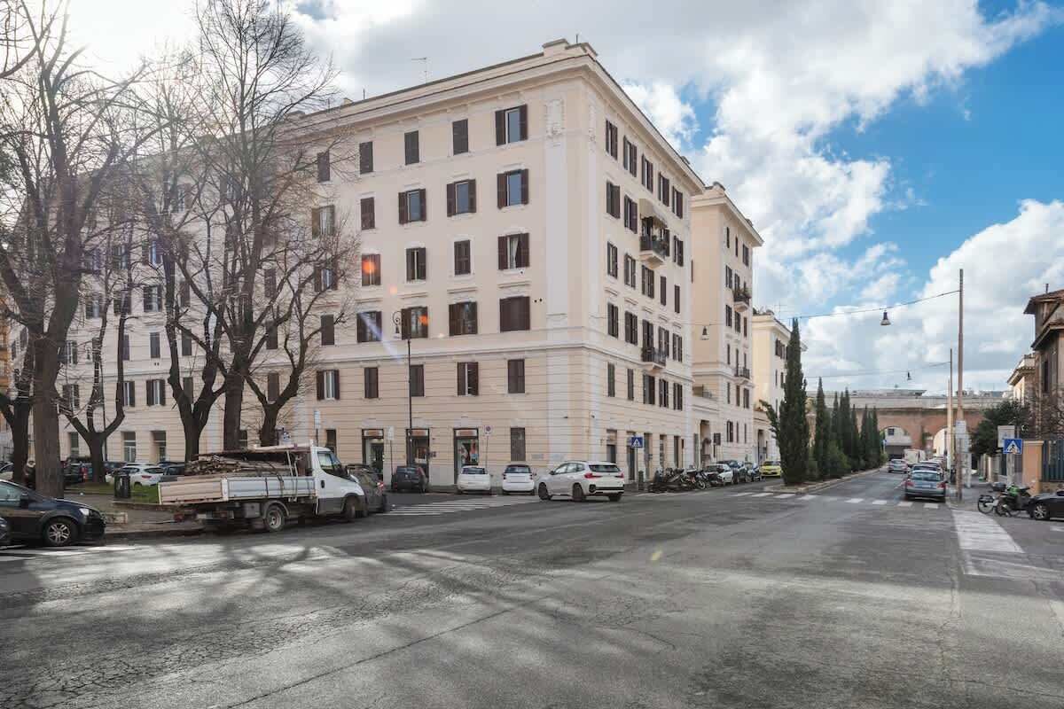 Ein mehrgeschossiges Gebäude mit flacher Fassade, geparkten Autos und blauem Himmel.