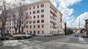 Ein mehrgeschossiges Gebäude mit flacher Fassade, geparkten Autos und blauem Himmel.