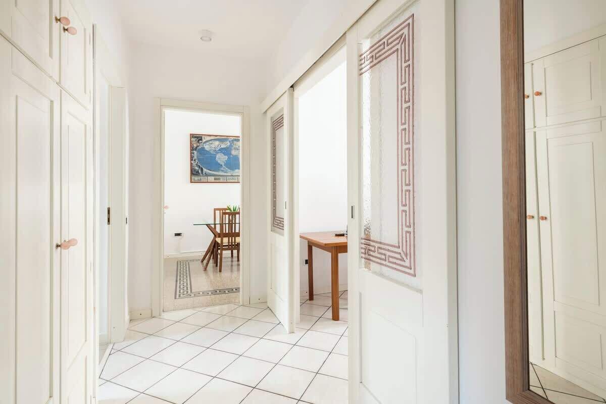 A hallway with white tiled flooring, a wooden table, and a framed picture on the wall.