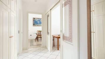 A hallway with white tiled flooring, a wooden table, and a framed picture on the wall.