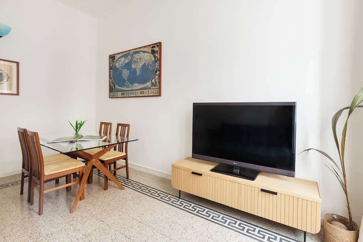 Un soggiorno con tavolo da pranzo in vetro, sedie di legno, una TV a schermo piatto su un mobile in legno, un quadro raffigurante un globo e una pianta in vaso.