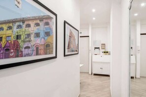 Ein Flur mit gerahmten Kunstwerken an den Wänden, ein heller Empfangsbereich und ein Blick auf einen Raum mit einem weißen Schrank.