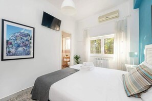 Ein Hotelzimmer mit Bett, Wandfernseher, Fenster mit Vorhängen und Heizkörper.