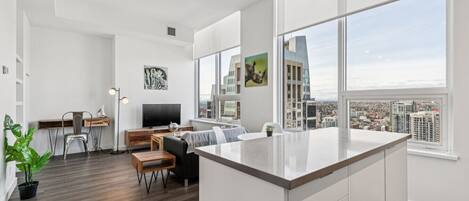 Un apartamento moderno con isla de cocina, comedor y un amplio ventanal con vistas a la ciudad.
