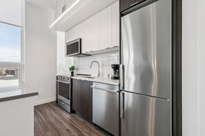 Une cuisine moderne dotée d’appareils électroménagers en acier inoxydable, de meubles blancs et offrant une vue sur la ville.