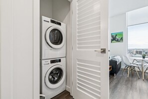 Une buanderie équipée de deux machines à laver et de deux sèche-linge à chargement frontal superposés, une porte blanche à lattes horizontales et une vue sur le paysage urbain par le biais d’une grande fenêtre.