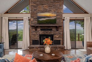 Una chimenea de piedra con vistas panorámicas, una mesa redonda de madera con un florero y un balcón con sillas.