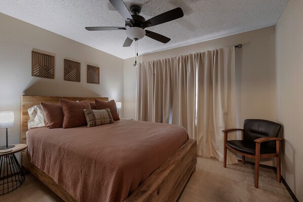 A bedroom with a bed, a chair, a ceiling fan, and curtains. - AR-MO-re. Table Rock Mountain views, minutes from Eureka Springs, dog friendly. (Holiday Island)