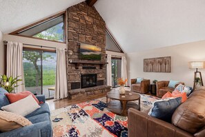 A spacious living room with a stone fireplace, large windows, and a cozy seating area.