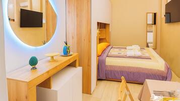 Una camera da letto moderna con una scrivania in legno, uno specchio rotondo, un letto con copriletto viola e giallo, e una sedia con un vassoio per la colazione.