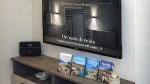 Un saló modern amb un televisor de pantalla plana fixat a la paret, un moble gris per a l'equipament de so i vídeo a la part inferior, i objectes decoratius sobre prestatgeries penjants.