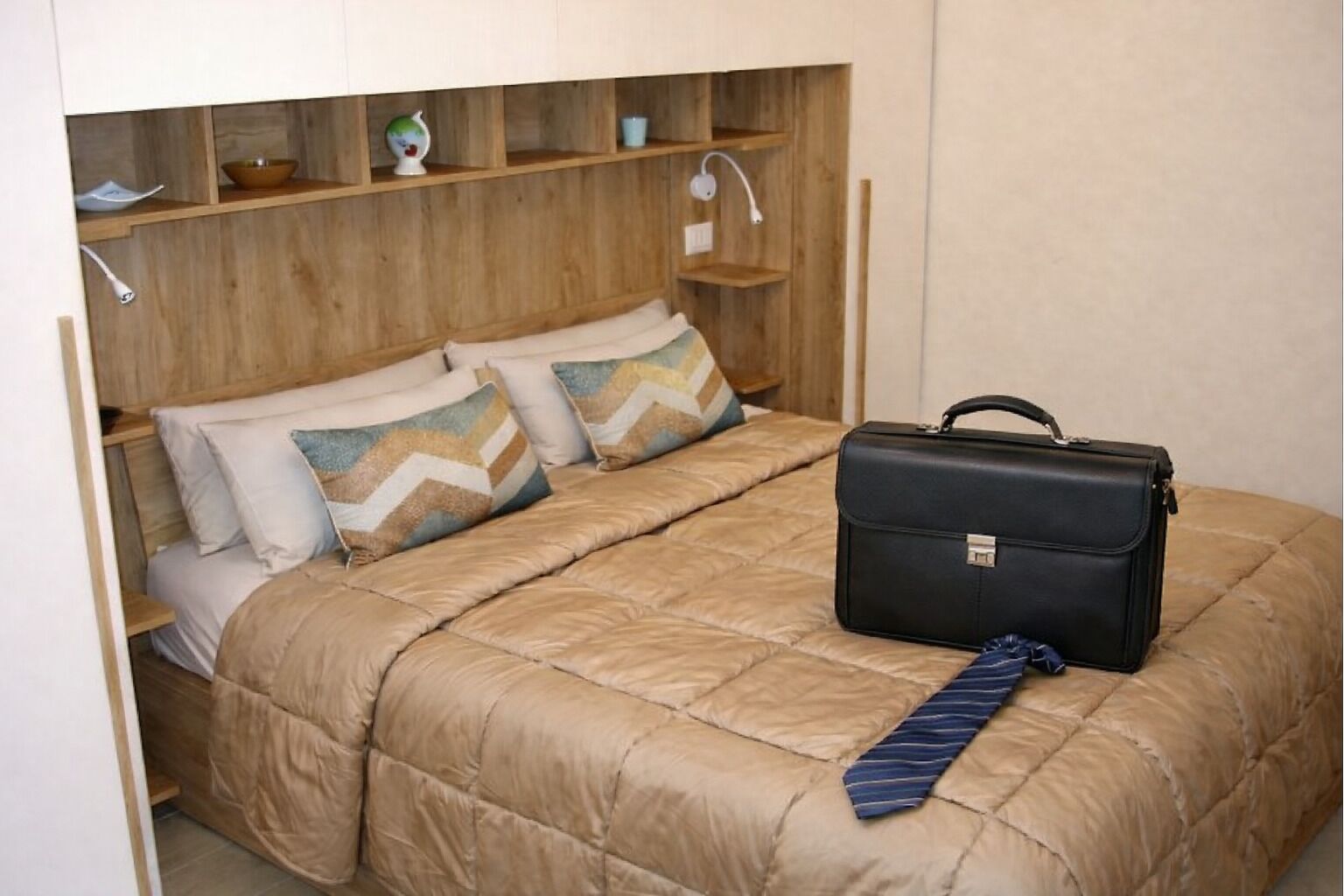 Uma cama compacta com cobertura acolchoada, uma mala preta e uma gravata listrada sobre a cama.