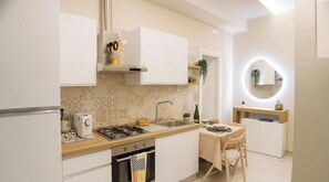Een moderne keuken met witte kastjes, een gasfornuis, een spoelbak en een klein zithoekje met een tafel en stoelen.
